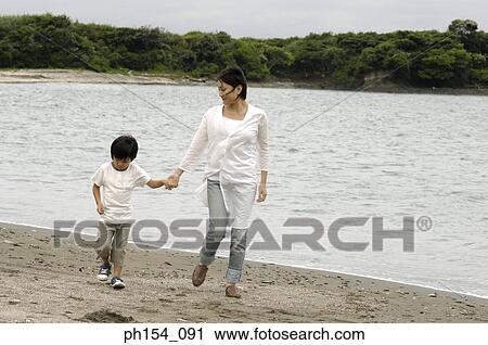 Stock Image - Mid adult woman walking with her son on the beach. Fotosearch