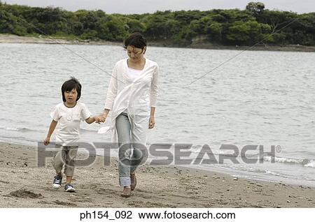 Stock Image - Mid adult woman walking with her son on the beach. Fotosearch