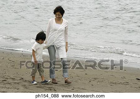 Stock Photo - Mid adult woman walking with her son on the beach. Fotosearch