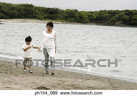 Stock Photo - Mid adult woman walking with her son on the beach. Fotosearch