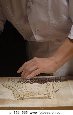 Stock Photography - Mid section view of a chef applying flour on raw noodles on a cutting board. Fotosearch