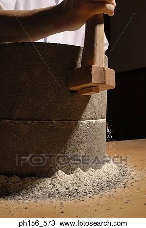 Stock Image - Mid section view of a person grinding grain in a grinding stone. Fotosearch