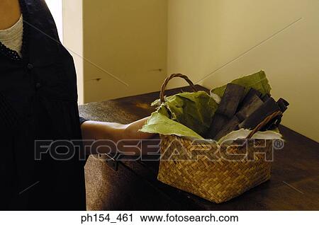 Stock Image - Mid section view of a woman holding a wicker basket with pieces of bamboo in it. Fotosearch