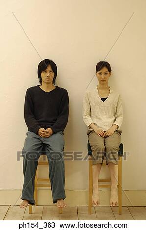 Stock Image - Portrait of a young couple sitting on stools. Fotosearch