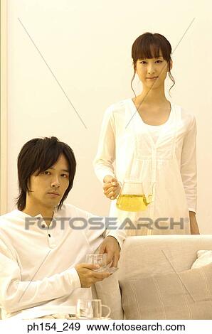 Stock Photo - Portrait of a young man holding a cup of tea with a young woman holding a teapot behind him. Fotosearch