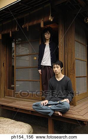 Stock Photograph - Portrait of a young man sitting with a young woman standing behind him. Fotosearch