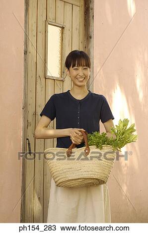 Portrait of a young woman holding a basket with vegetables and smiling View Large Photo Image Stock Image - Portrait of a young woman holding a basket with vegetables and smiling. Fotosearch