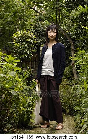 Portrait of a young woman standing in a garden View Large Photo Image Stock Photo - Portrait of a young woman standing in a garden. Fotosearch
