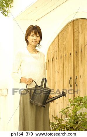 Stock Photo - Portrait of a young woman watering plants with a watering can. Fotosearch