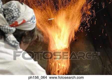 Picture - Rear view of a blacksmith in front of a furnace. Fotosearch