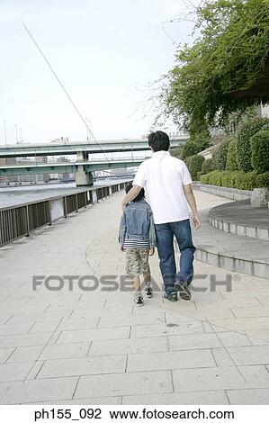 Stock Image - Rear view of a father and his son walking with their arms around each other. Fotosearch