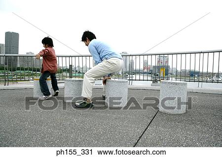 Rear view of a mid adult man and his son playing on concrete seats View Large Photo Image Stock Image - Rear view of a mid adult man and his son playing on concrete seats. Fotosearch