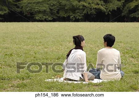 Stock Photograph - Rear view of a young couple sitting together on a mat. Fotosearch
