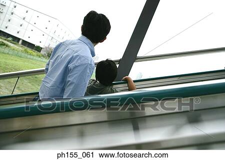Stock Image - Rear view of a young man and his son on an escalator. Fotosearch