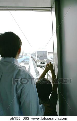 Stock Image - Rear view of a young man and his son looking at a train. Fotosearch