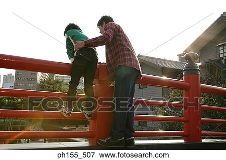 Rear view of a young man and his son leaning on a railing and looking down View Large Photo Image Stock Photo - Rear view of a young man and his son leaning on a railing and looking down. Fotosearch