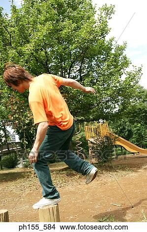 Picture - Rear view of a young man jumping on a wooden post. Fotosearch