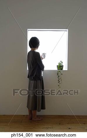 Rear view of a young woman holding a coffee cup and standing near a window View Large Photo Image Stock Image - Rear view of a young woman holding a coffee cup and standing near a window. Fotosearch