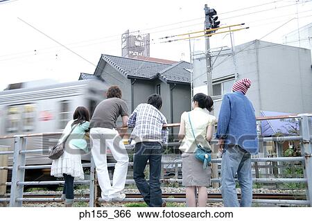 Stock Photograph - Rear view of three men and two women leaning against a railing. Fotosearch