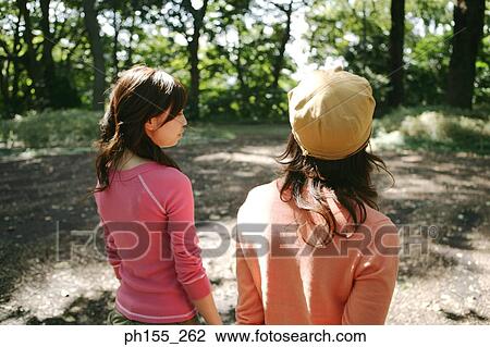 Stock Image - Rear view of two young women standing in a park. Fotosearch