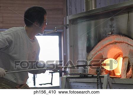 Stock Image - Side profile of a mid adult man molding a glass bulb. Fotosearch