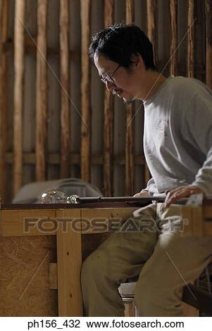 Stock Image - Side profile of a mid adult man molding a glass bulb. Fotosearch