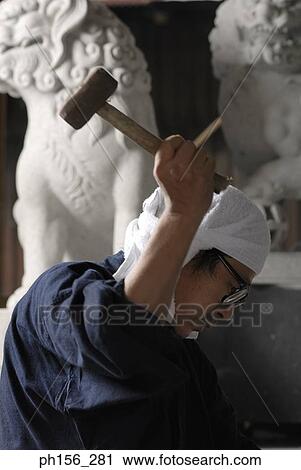 Stock Image - Side profile of a sculptor using a hammer. Fotosearch