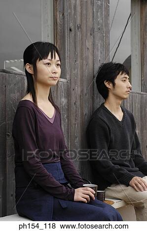 Stock Photo - Side profile of a young couple sitting on a bench. Fotosearch