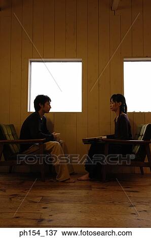 Stock Photo - Side profile of a young couple sitting near windows. Fotosearch