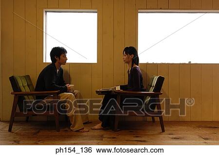 Stock Photograph - Side profile of a young couple sitting near windows. Fotosearch