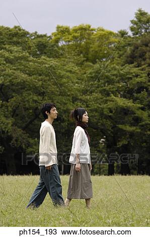 Stock Image - Side profile of a young couple walking together. Fotosearch
