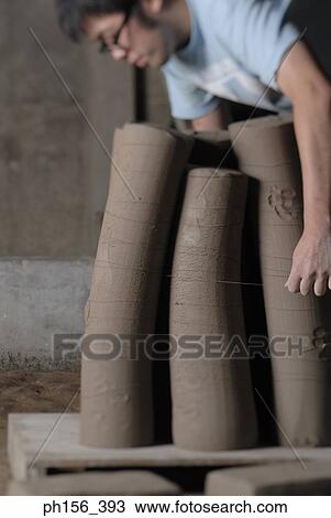 Stock Image - Side profile of a young man dividing blocks of clay with string. Fotosearch