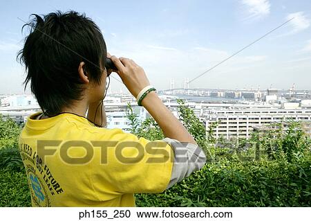 Stock Image - Side profile of a young man looking through a pair of binoculars. Fotosearch