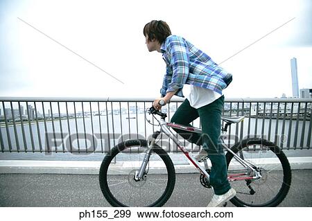 Side profile of a young man riding a bicycle View Large Photo Image Stock Photo - Side profile of a young man riding a bicycle. Fotosearch