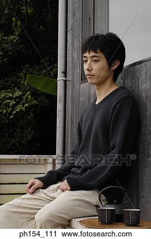Stock Image - Side profile of a young man sitting on a bench. Fotosearch