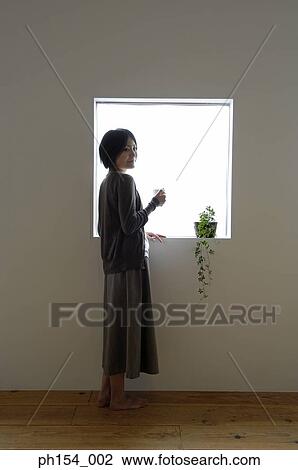 Side profile of a young woman holding a coffee cup and standing near a window View Large Photo Image Stock Image - Side profile of a young woman holding a coffee cup and standing near a window. Fotosearch