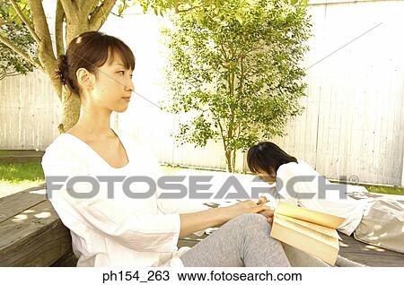 Stock Image - Side profile of a young woman holding a book with a young man lying beside her. Fotosearch