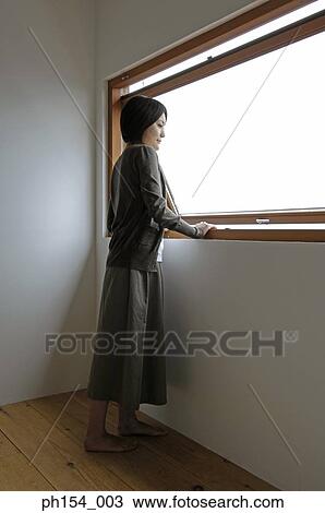 Stock Image - Side profile of a young woman looking through a window. Fotosearch