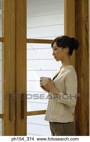 Side profile of a young woman standing and holding a cup of coffee View Large Photo Image Picture - Side profile of a young woman standing and holding a cup of coffee. Fotosearch