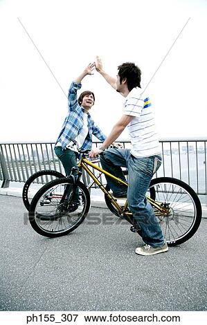 Side profile of two young men sitting on a bicycle and giving high-five View Large Photo Image Stock Photo - Side profile of two young men sitting on a bicycle and giving high-five. Fotosearch