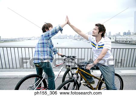 Side profile of two young men sitting on a bicycle and giving high-five View Large Photo Image Stock Photograph - Side profile of two young men sitting on a bicycle and giving high-five. Fotosearch