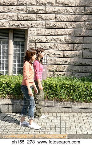 Stock Photo - Side profile of two young women walking on a footpath. Fotosearch