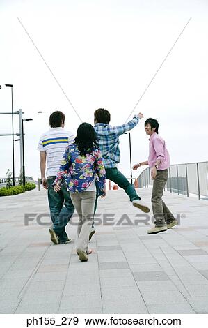Stock Photo - Three young men and a young woman walking on the road. Fotosearch