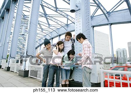 Stock Image - Three young men and two young women looking at a map. Fotosearch