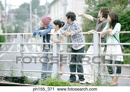 Stock Image - Three young men and two young women leaning against a railing. Fotosearch