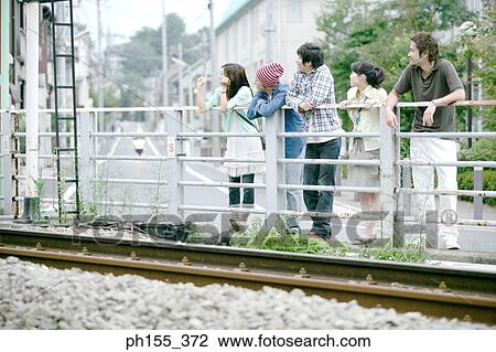 Three young men and two young women leaning against a railing View Large Photo Image Stock Image - Three young men and two young women leaning against a railing. Fotosearch