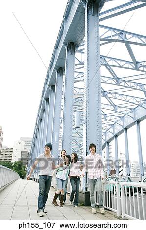 Three young men and two young women smiling and walking together on a bridge View Large Photo Image Stock Photo - Three young men and two young women smiling and walking together on a bridge. Fotosearch