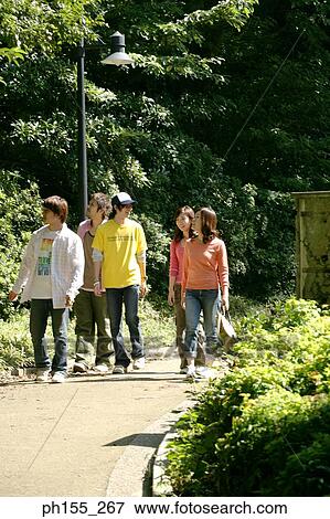 Stock Photo - Three young men and two young women walking in a park. Fotosearch