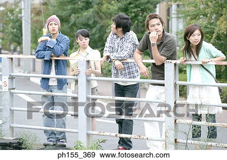 Stock Photo - Three young men and two young women leaning against a railing. Fotosearch