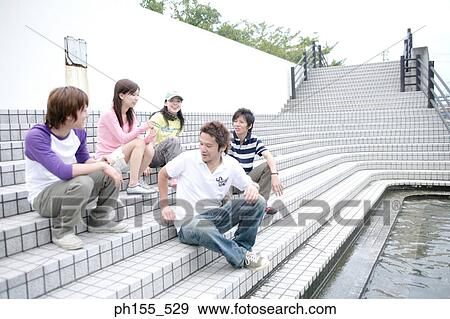 Three young men and two young women sitting at the poolside and talking View Large Photo Image Stock Photo - Three young men and two young women sitting at the poolside and talking. Fotosearch